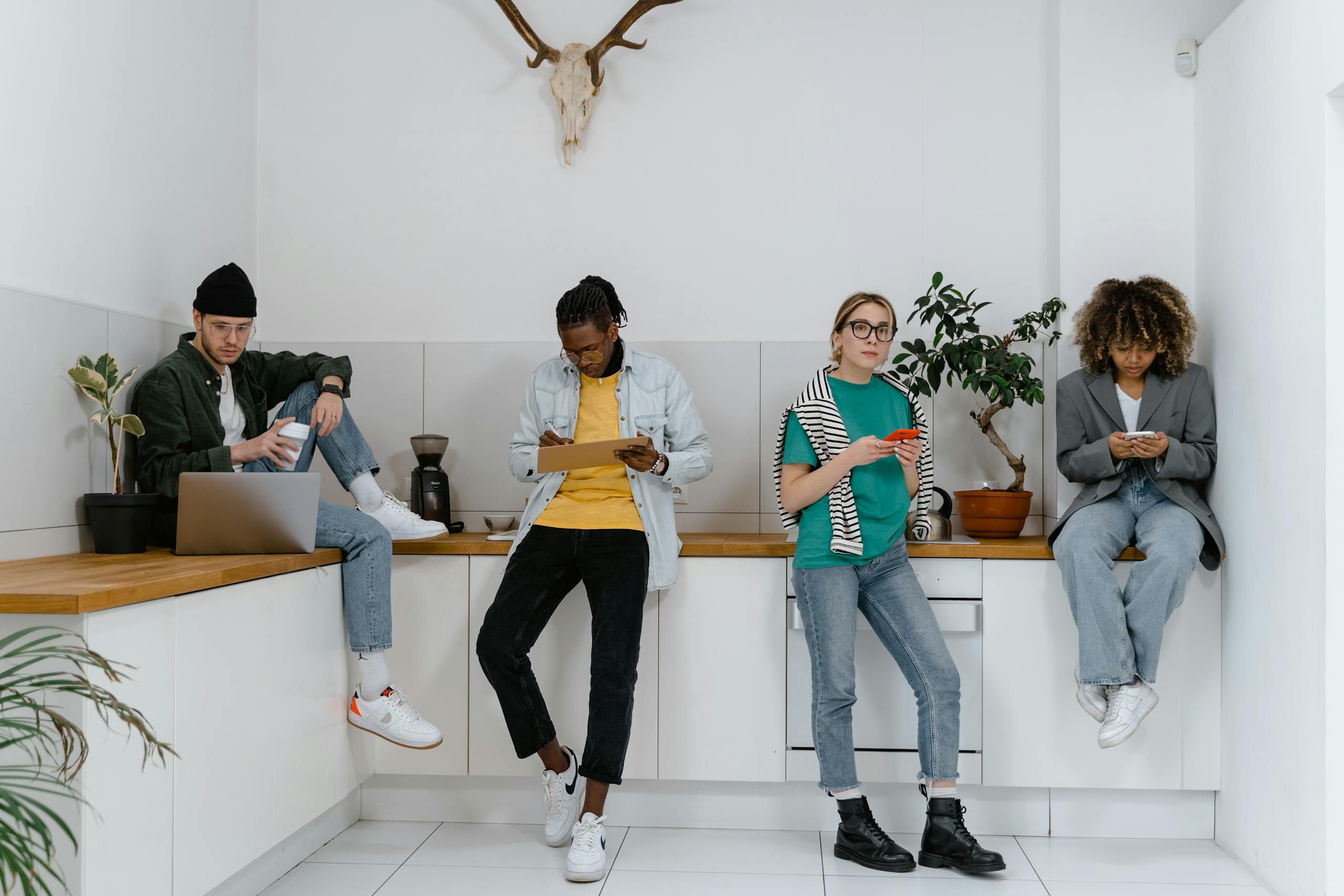 Casual and diverse colleagues using gadgets in a modern office kitchen area.