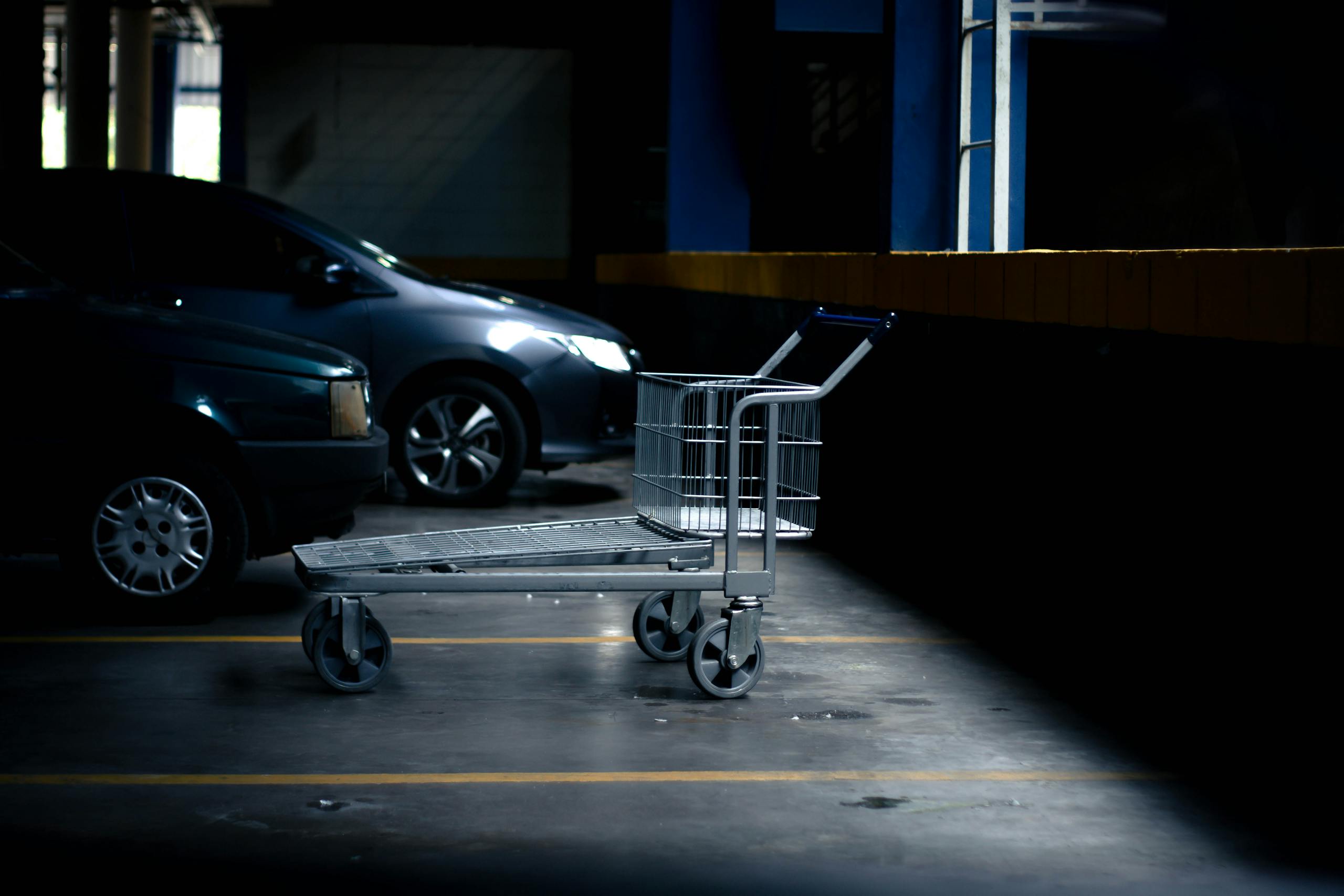 Lonely shopping cart in a dimly lit parking garage next to parked cars.