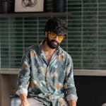 Portrait of a man in a floral shirt with sunglasses, sitting indoors near a billiard table.
